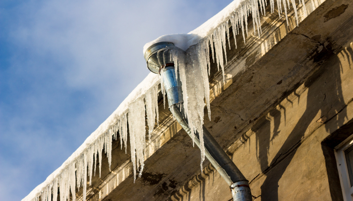 Thick cicles on the roof of the building, rainwater pipe overgrown with ice on winter season