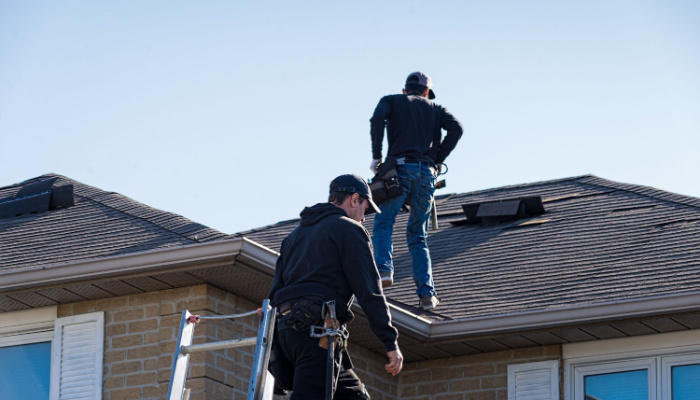 Two professional roofers inspecting a damaged roof after winter season