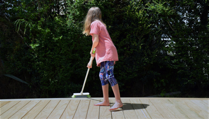 girl in pink shirt sweeps the outside deck at her house