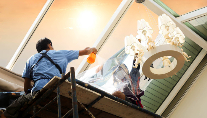 construction worker tinting a glass house window with tinted foil or film using foggy spray