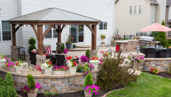 Colorful exterior curved patio with summer flowers and comfortable chairs under a covered wooden gazebo with aluminum roof in a neat upscale backyard