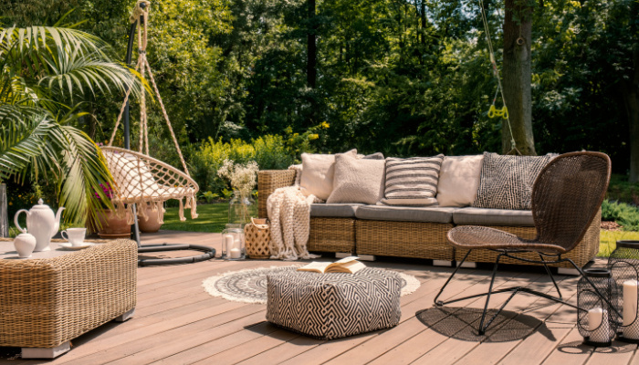 A cozy rattan patio set with a hanging chair, sofa, a table and a chair on a wooden deck in the sunny garden in the fall season